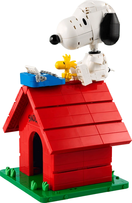 Brick built LEGO Snoopy seated on the red doghouse roof beside Woodstock and a blue typewriter, with the model on a green base.