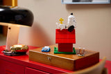 LEGO Snoopy and Woodstock displayed on the red doghouse atop a wooden box, with the blue typewriter and campfire scene placed beside it.
