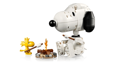 LEGO Snoopy seated opposite yellow Woodstock beside a small campfire, with both characters holding roasting sticks.