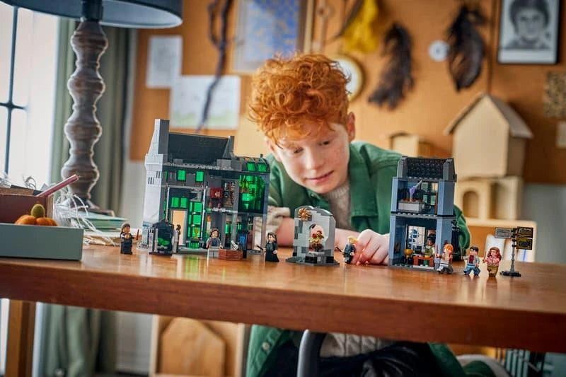 Child building a LEGO Harry Potter wizarding shops set at a table with shop models, minifigures and tablet instructions