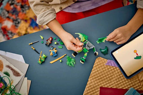 Child building a LEGO NINJAGO dragon mech set on a table with green wing pieces, minifigures and tablet instructions