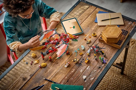 Child building a LEGO NINJAGO dragon mech set on a table with pieces, minifigures and tablet instructions