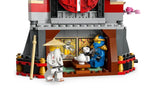 Rear view of the LEGO NINJAGO monastery display showing the open tearoom area with table, teapot, wall stickers depicting a battle scene, and two minifigures.
