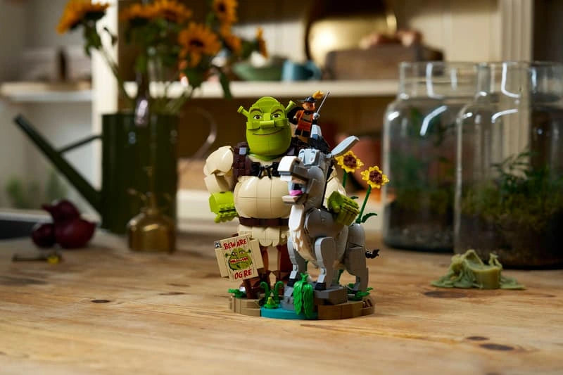 LEGO Shrek, Donkey & Puss in Boots 72423 assembled model displayed on a wooden table with sunflowers and a Beware Ogre sign.