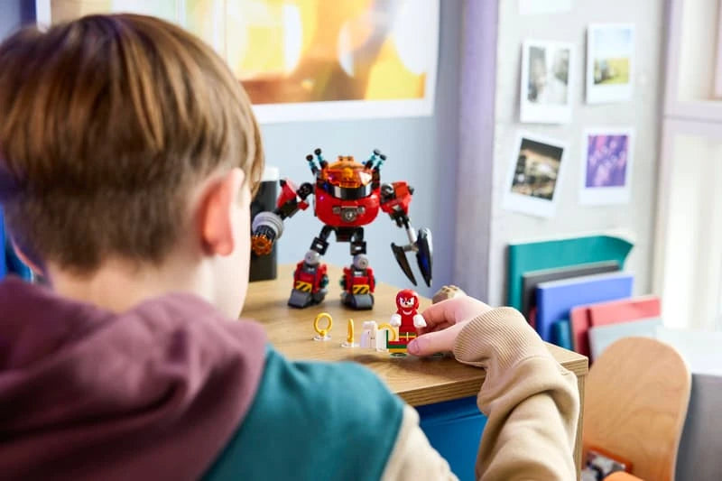 Child moving the Knuckles figure beside the LEGO Egg Crusher Mech and three Gold Rings on a desk 