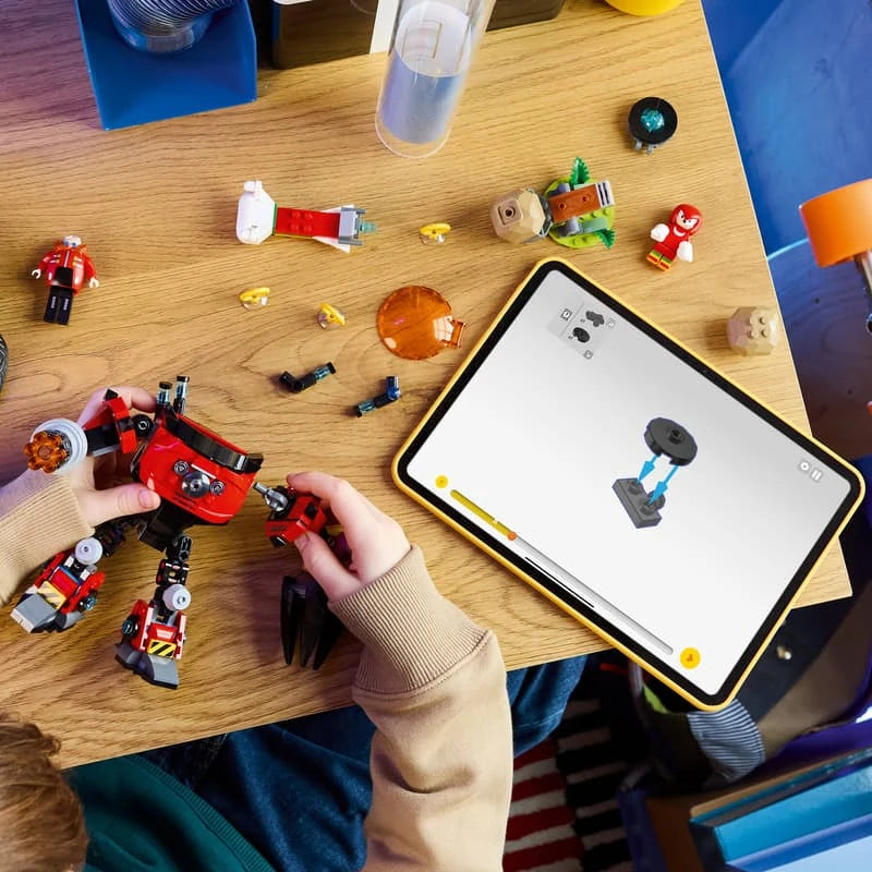 Child assembling the LEGO Egg Crusher Mech at a wooden table with loose pieces and digital instructions displayed on a tablet