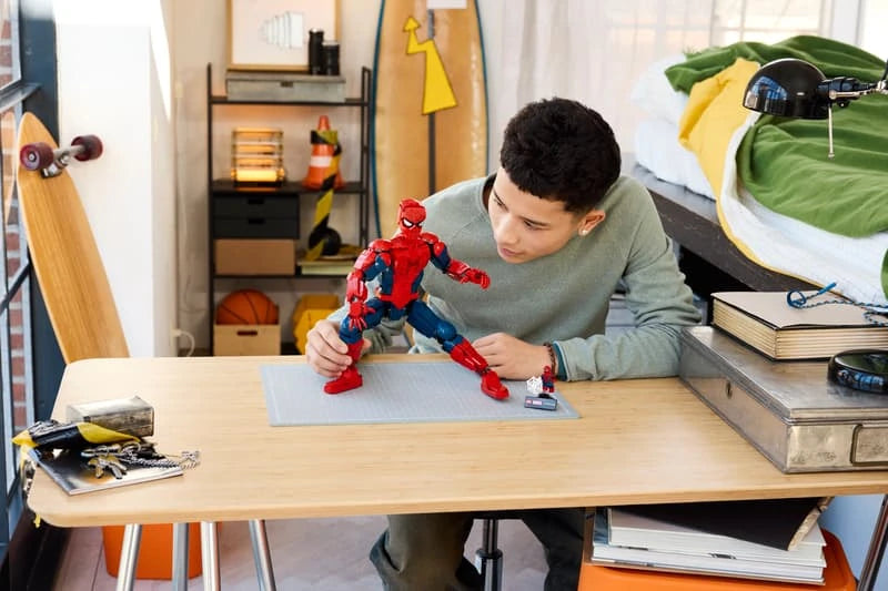 Child posing a LEGO Spider-Man figure on a desk