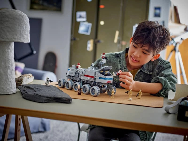 Child moving a red and white clone trooper beside the LEGO Star Wars Republic Juggernaut on a wooden table