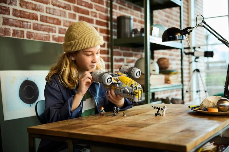 Woman holding the LEGO Star Wars The Razor Crest above a wooden table with Grogu and minifigures positioned below