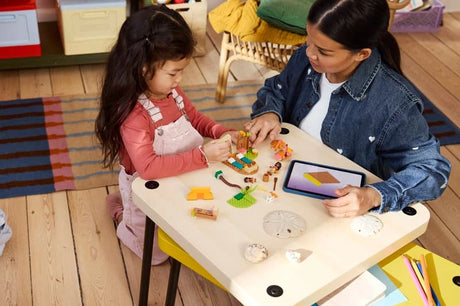 Child and adult building LEGO Village House & Boat on a table with a tablet nearby