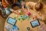 Two children building LEGO Water Lilies at a table with loose pieces and tablets visible