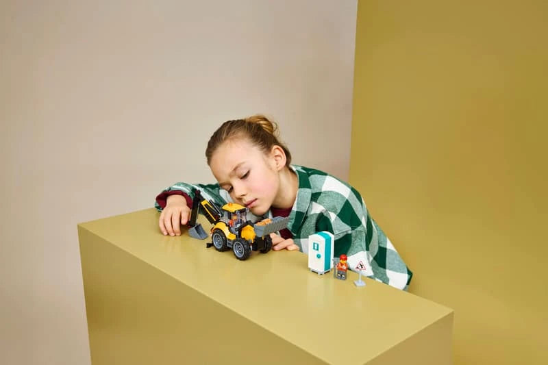 Child playing with LEGO Yellow Backhoe Loader on a table with portable toilet build nearby