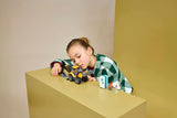 Child playing with LEGO Yellow Backhoe Loader on a table with portable toilet build nearby