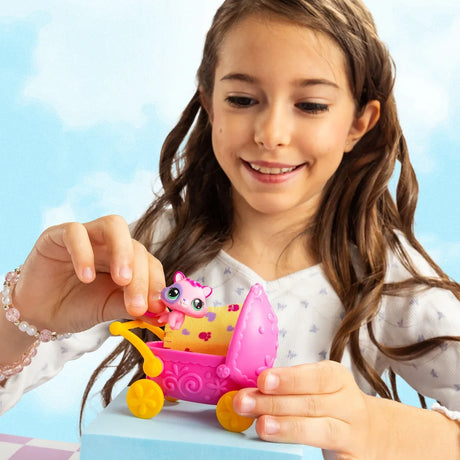 Girl placing a small pink and white Littlest Pet Shop cat into a bright pink baby pram with yellow wheels and raised hood.