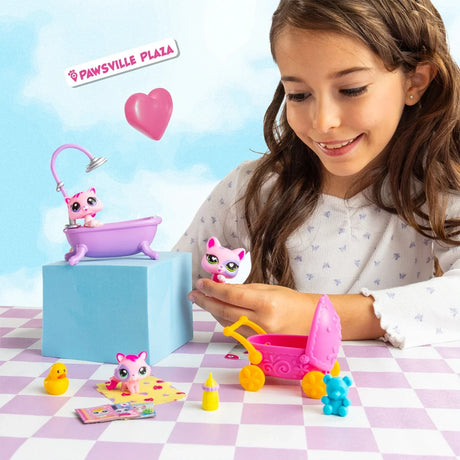 Girl playing with Littlest Pet Shop cat figures beside a purple bathtub with shower attachment and a pink baby pram, with miniature bath accessories arranged nearby.