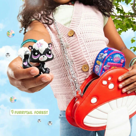 Close-up of a child holding two black and white Littlest Pet Shop animal figures beside a bright red bag decorated with white spots.