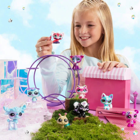 Smiling girl holding a pink Littlest Pet Shop figure beside a pink striped display with several colourful animal figures.