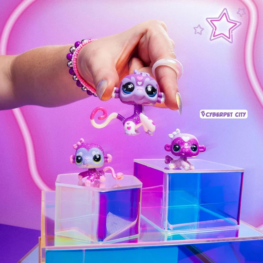 Purple Littlest Pet Shop monkey mother and baby figures displayed on colourful transparent blocks, with a hand holding the larger monkey figure above the others.