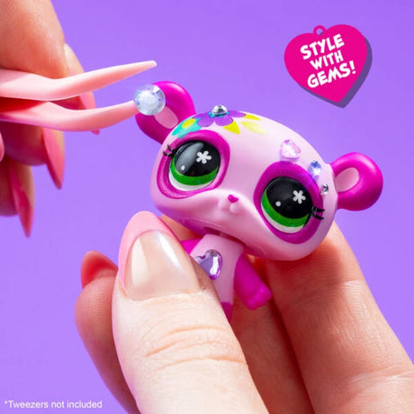 Close-up of a purple and pink Littlest Pet Shop panda figure being decorated with a small gem using pink tweezers.