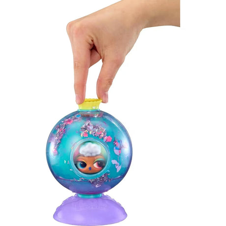 L.O.L. Surprise Bubbly Surprise Tot doll's face visible through the circular window of a turquoise capsule filled with colourful confetti, with a hand holding the yellow cap.