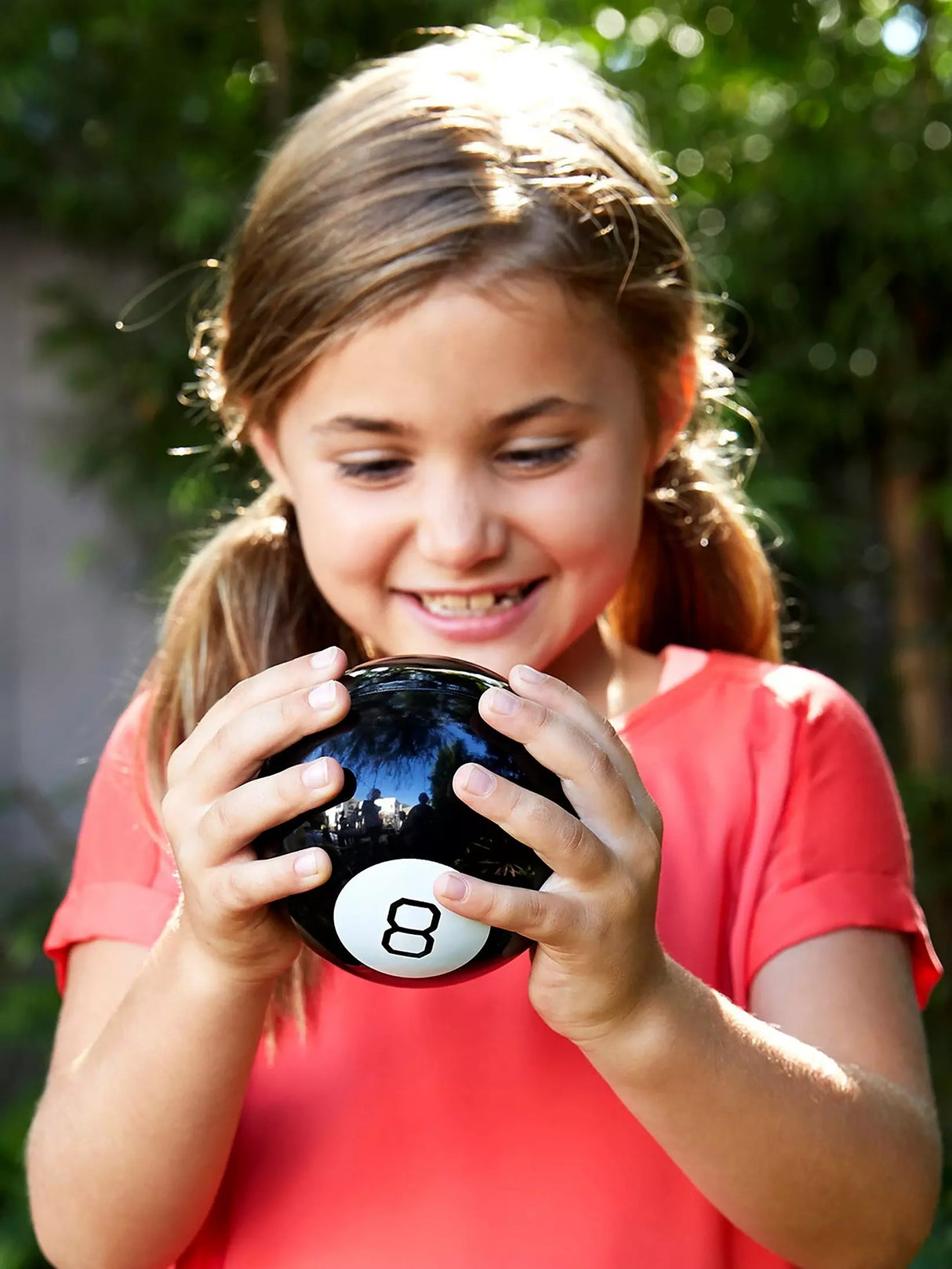 Child holding a black Magic 8 Ball close to her face outdoors