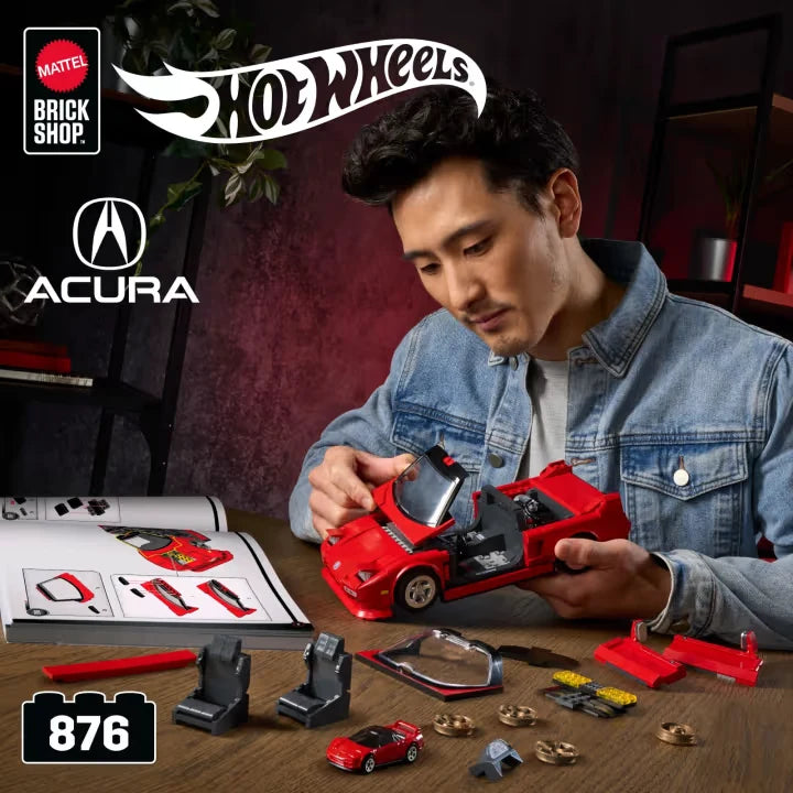 Person assembling a red Hot Wheels Acura NSX model beside instructions, tools, small parts and a 1:64 car