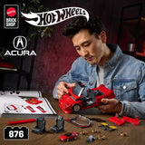 Person assembling a red Hot Wheels Acura NSX model beside instructions, tools, small parts and a 1:64 car