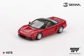 Mini GT Honda NS-X Ayrton Senna model photographed from the front three quarter angle, showing the red bodywork, black roof and seated driver wearing a yellow and green helmet