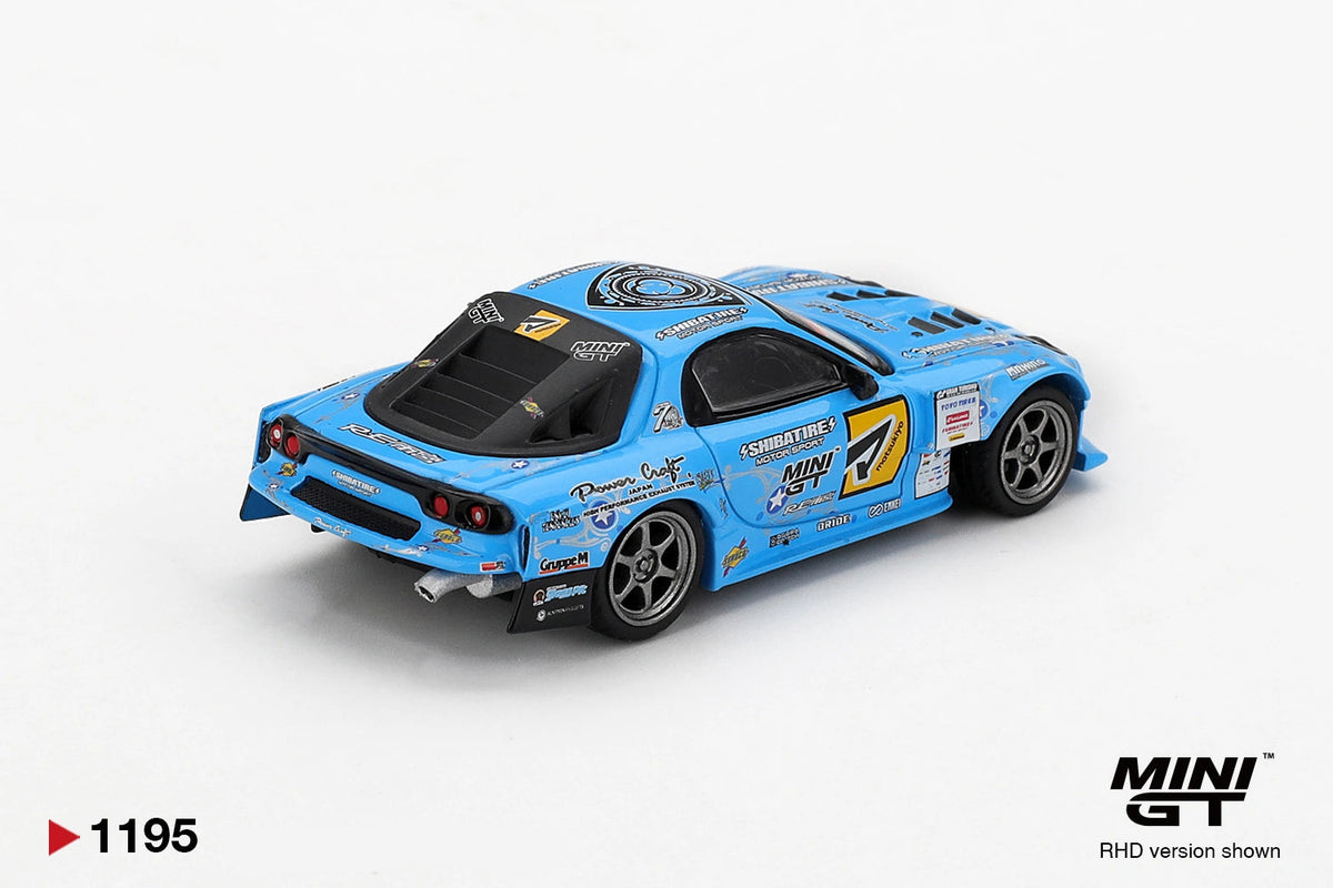 Rear three quarter view of Mini GT Mazda RX-7 RE-Amemiya 2025 D1GP RHD showing round rear lights, black rear bumper, exhaust pipe, silver wheels and blue racing graphics