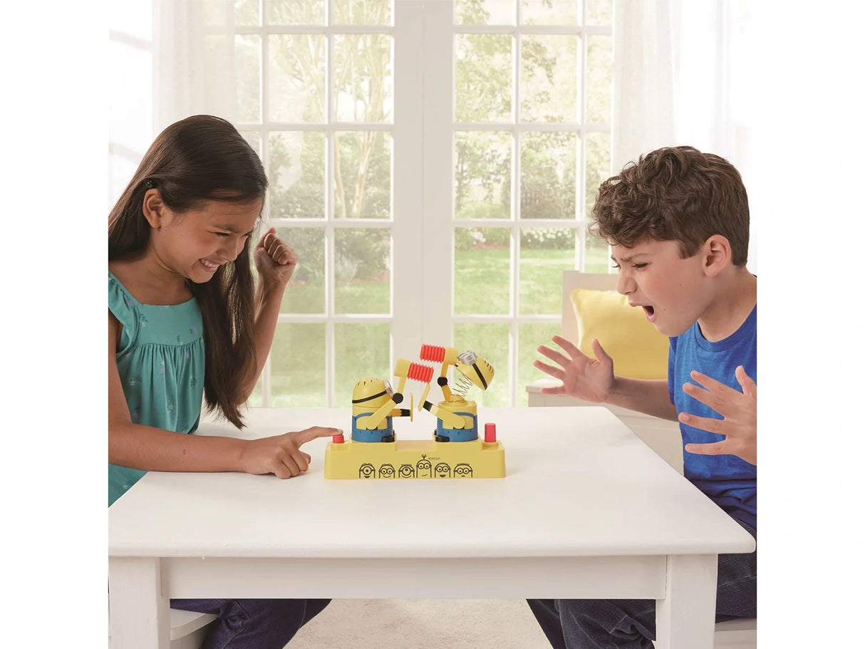 Two children sitting at a table with the Minions Hammer POP game between them