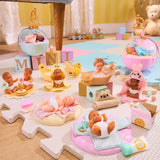 Collection of Miniverse Real Baby Nurture miniature babies arranged on a playroom floor, featuring babies in bassinets with hanging mobiles, a foam filled bath, bunny hooded towels, changing mats, stacking ring toys and miniature baby care accessories.