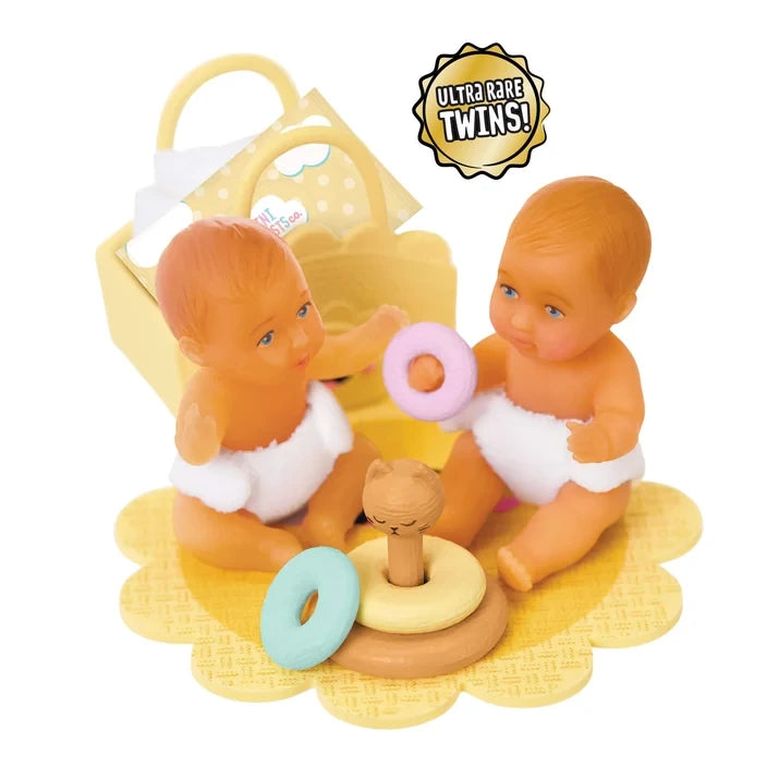 Two Miniverse Real Baby Nurture miniature twin babies wearing white nappies and sitting on a yellow mat with pastel stacking rings and a small animal toy, with a yellow accessory basket behind them and an Ultra Rare Twins badge above.