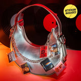 Silver handbag decorated with miniature album cover keychains featuring artists including TLC, Britney Spears and Imagine Dragons, against a background of black vinyl records.