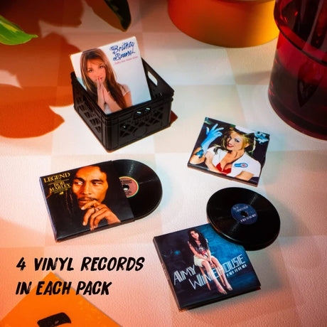 Four miniature album sleeves and black vinyl records featuring music artists including Britney Spears, Bob Marley and Amy Winehouse, arranged beside a miniature record crate with promotional text stating four records in each pack.