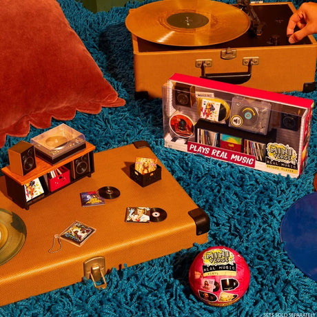 Miniverse Real Music promotional scene showing a boxed miniature record player, tiny vinyl records and album sleeves arranged on a suitcase beside a pink Real Music surprise capsule. Record player sold separately.
