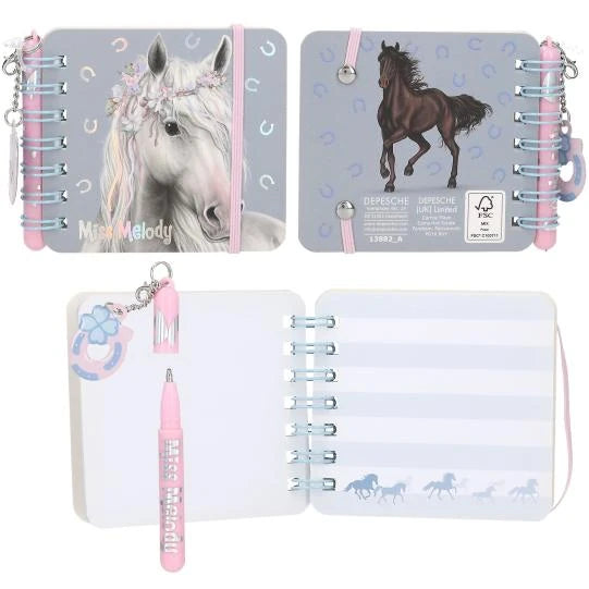 Miss Melody mini notebook with a white horse on the cover, a dark horse on the back, open striped pages and a pink pen.
