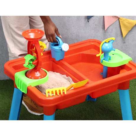 Child using a watering can at the Multiplay Table With Toys with sand in one side of the table