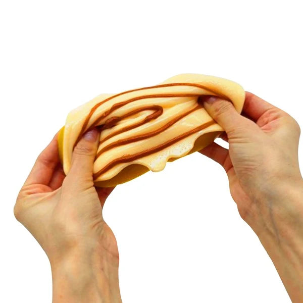 Mushmeez Taba Squishy cinnamon roll design stretched between two hands showing the layered filling