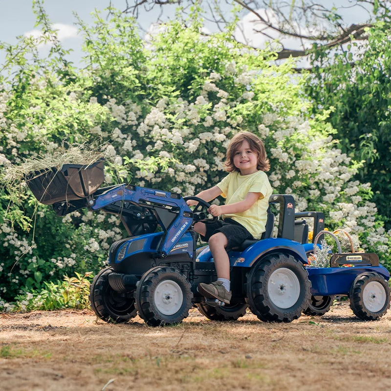 Child driving New Holland Blue backhoe with trailer in garden setting – Ireland