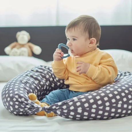 Baby chewing Nuvita blue teether while sitting on a patterned cushion