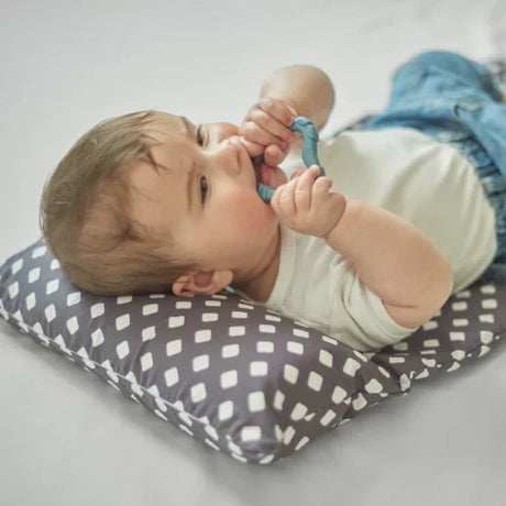 Baby lying on a patterned cushion holding Nuvita blue teether