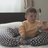 Baby sitting on a patterned cushion holding Nuvita blue teether