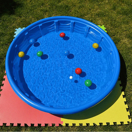 Blue round rigid plastic paddling pool filled with water and colourful balls placed on interlocking foam play mats on grass outdoors