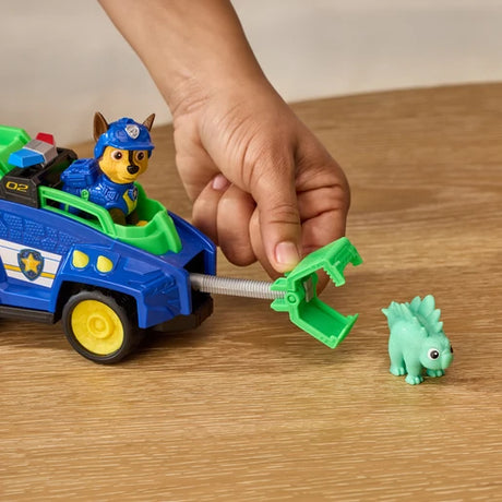 Hand operating the rescue claw on the PAW Patrol Chase Dino Rescue Cruiser beside the green dinosaur figure