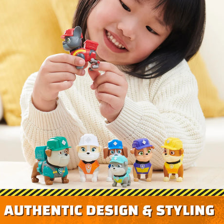 Child holding a Rubble & Crew figure with other pup figures lined up on a table