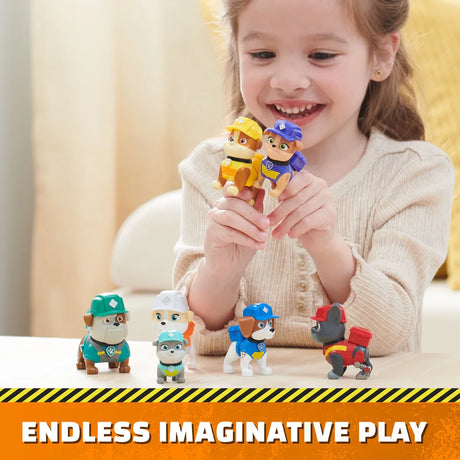 Child holding Rubble and another Rubble & Crew figure with other pup figures on the table