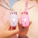 Two hands holding a lilac and a pink Peekimo interactive pet, both peeking out of their open pods with glowing star shaped lights and patterned neck straps.