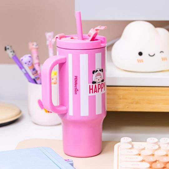 PENfection HAPPY cup with pink straw and handle standing on a desk beside stationery