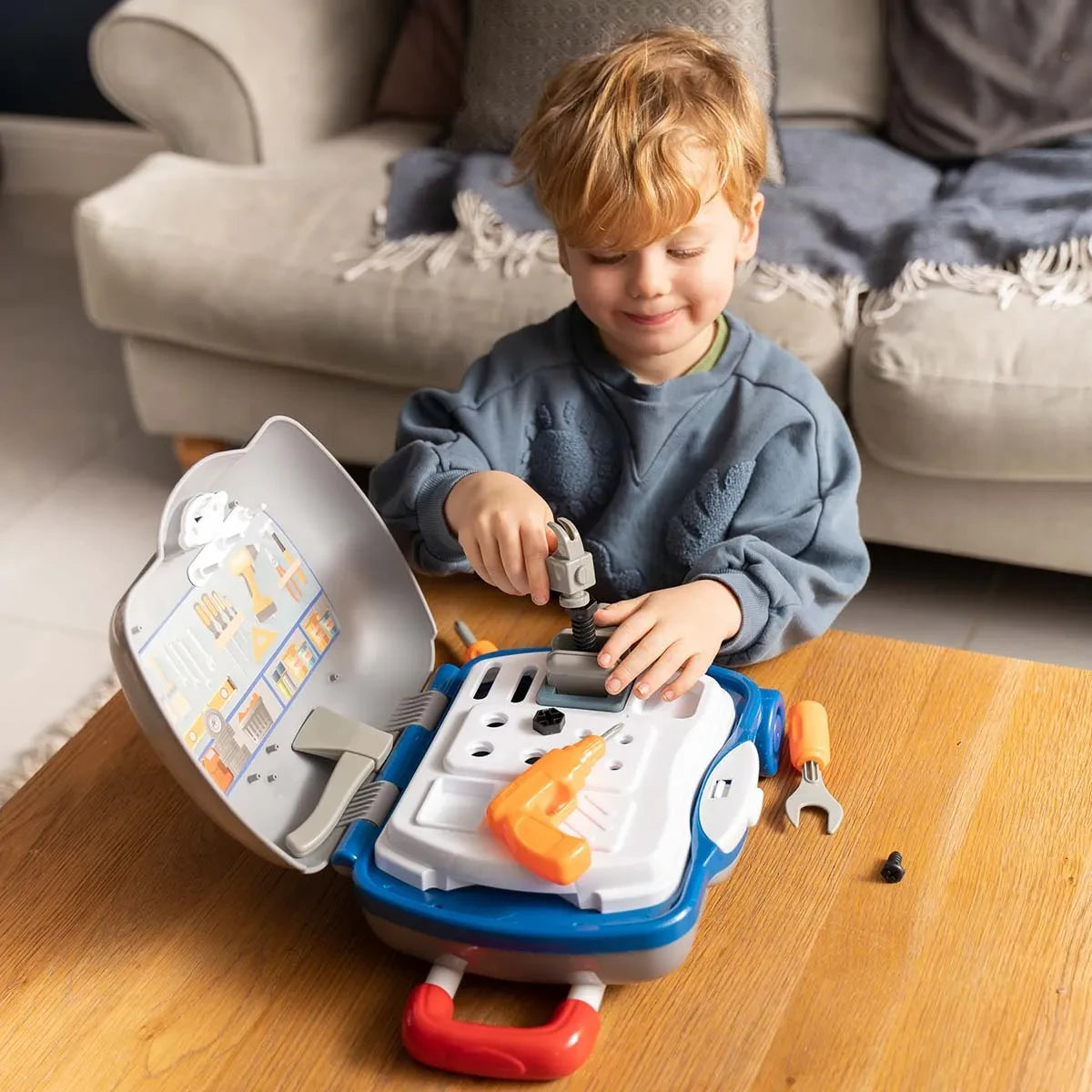 Child turning the handle of the grey vice on the open Little Workshop Suitcase with an orange toy drill and spanner beside it