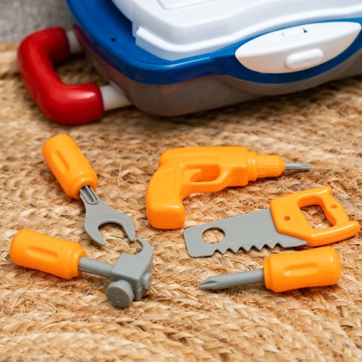 Orange toy drill, grey spanner, orange and grey saw, grey hammer and two orange screwdrivers arranged beside the suitcase